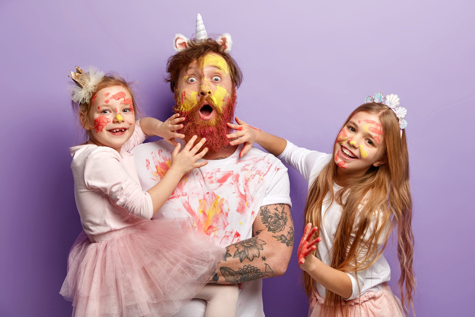 Père qui joue avec ses deux filles à à se mettre de la peinture partout, le père porte un serre-tête licorne